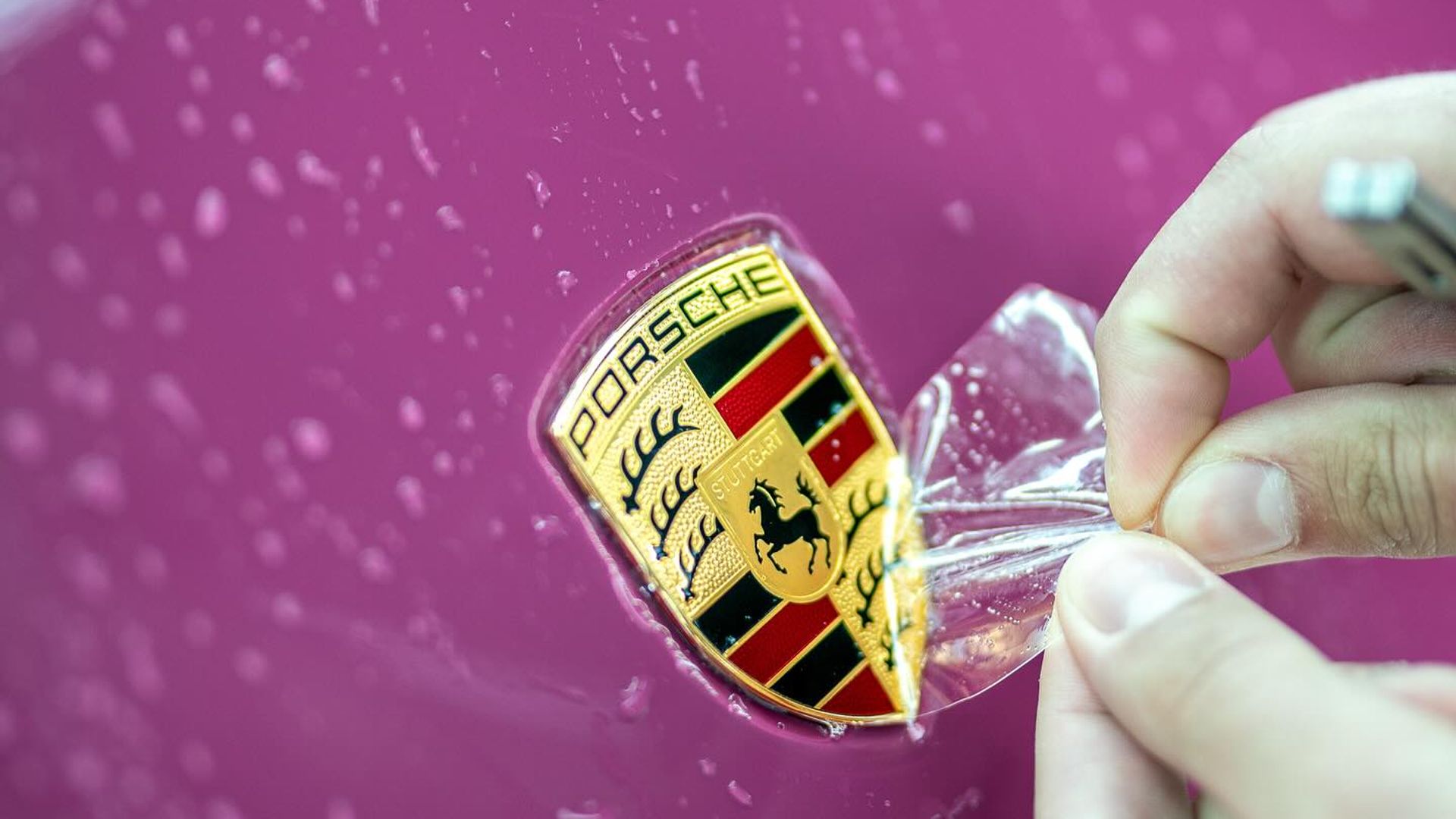 PPF film being applied around the Porsche badge on a ruby red Porsche